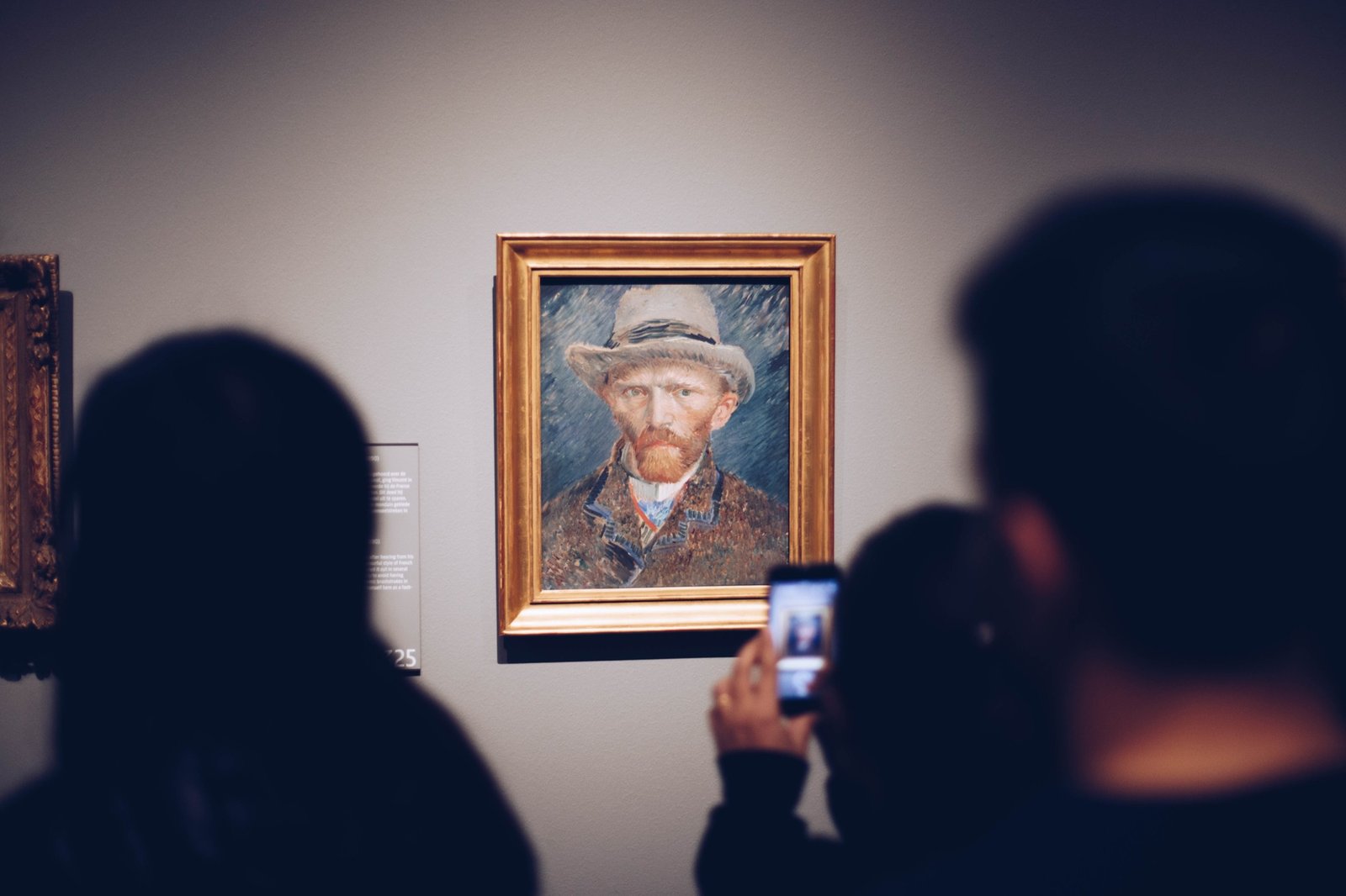 Two visitors photographing Van Gogh's self-portrait in its gold
                 frame.