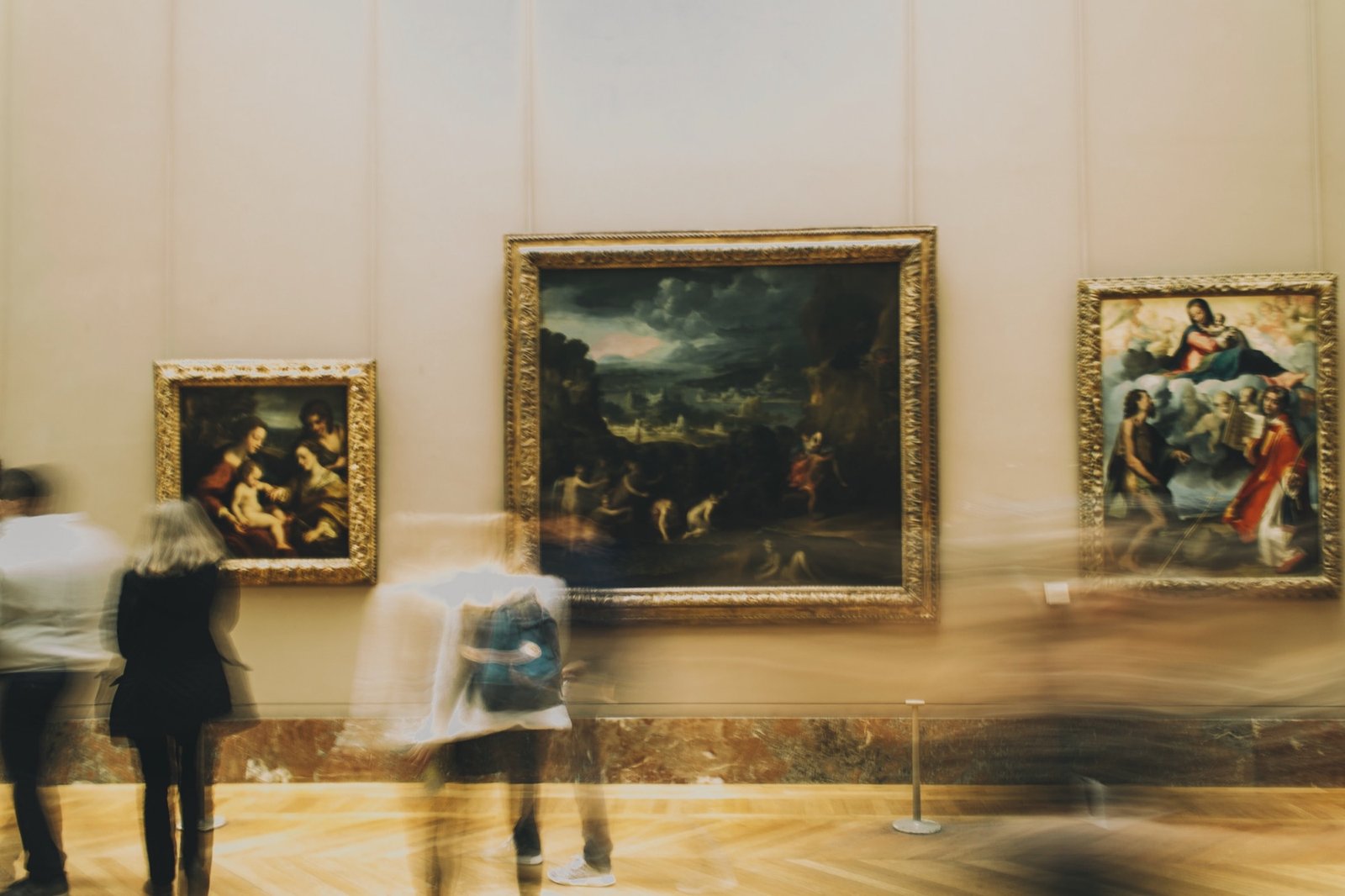 Visitors moving past gilded old-master paintings in a museum
                 gallery, caught in a long exposure.