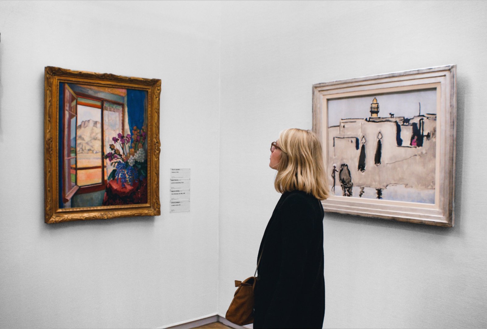 Scratcher — a visitor studying two framed paintings on
                         a white gallery wall.