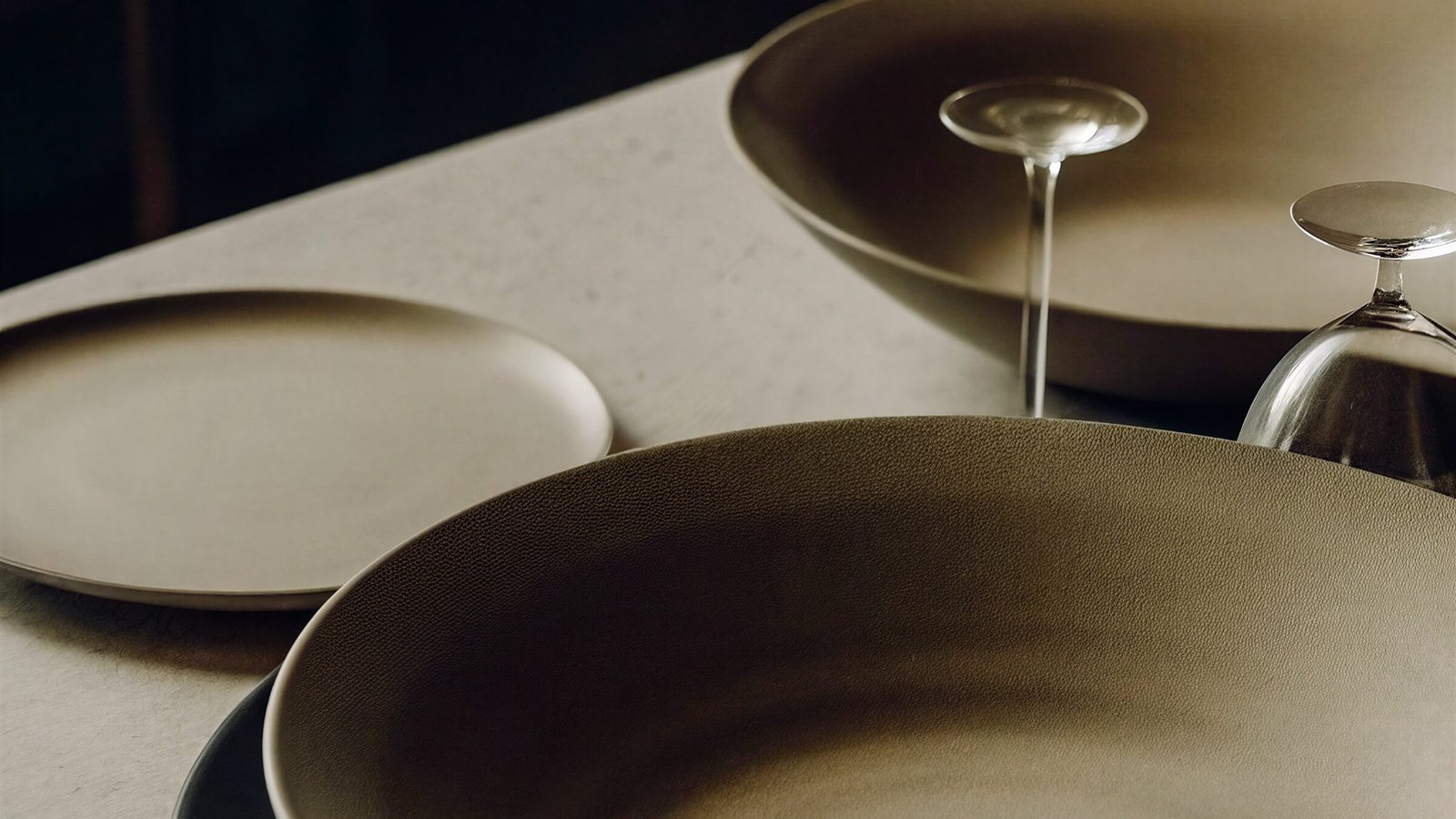 Two plates and an upturned wine glass on a pale stone table, lit low and warm.